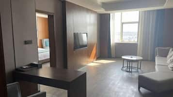 A modern hotel room with a bed, a desk, a TV, a round coffee table, and a sofa.