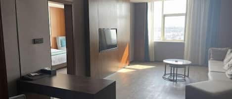 A modern hotel room with a bed, a desk, a TV, a round coffee table, and a sofa.
