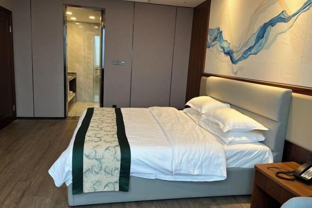 Habitación de hotel con una cama grande, una mesita de noche con teléfono y una pared con un cuadro abstracto azul.