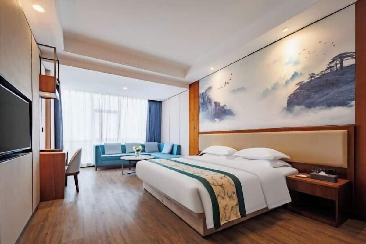 A hotel room with a large bed, a desk, a chair, a sofa, and a painting on the wall.