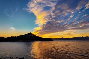 A sunset over a body of water with a silhouette of a hill and a lighthouse.