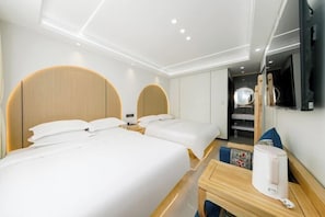 A hotel room with two beds, a wooden headboard, a bedside table with a coffee maker, and a mirror on the wall.