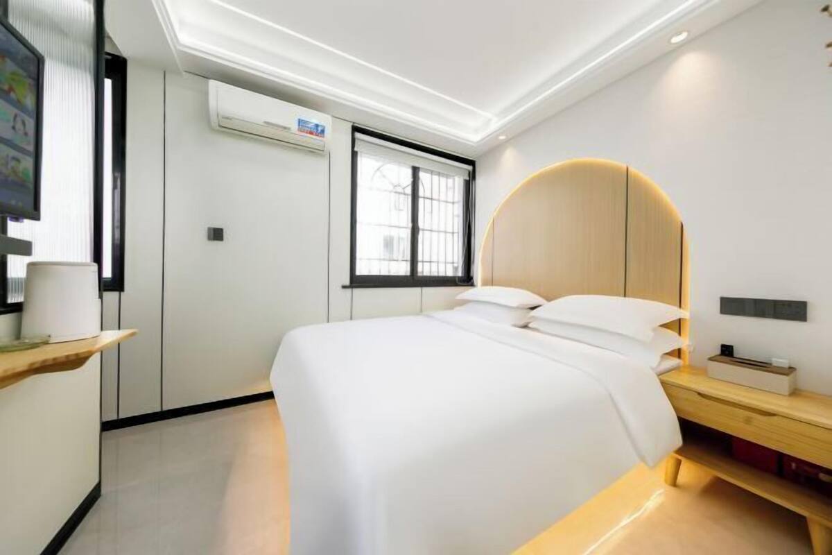 A modern hotel room with a bed, bedside table, and a built-in circular light fixture.