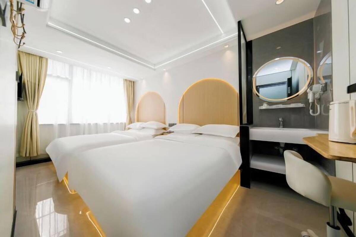 A hotel room with a large bed, a bedside table, a mirror, and a view of the outside.