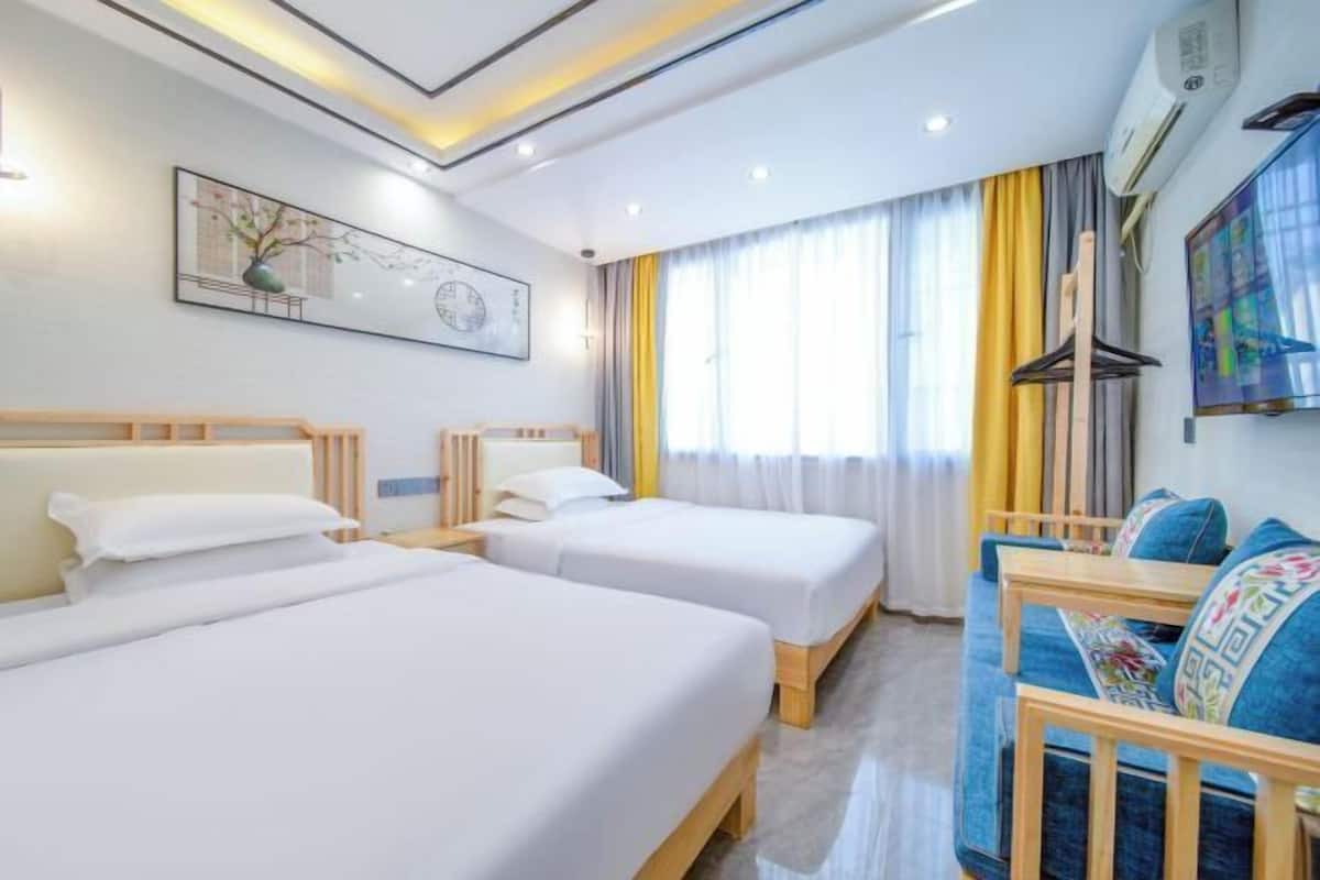 A hotel room with two beds, a sofa, a painting, and a window with curtains.