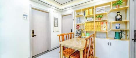 A dining area with a wooden table and chairs, a bookshelf with various items, and a door to another room.
