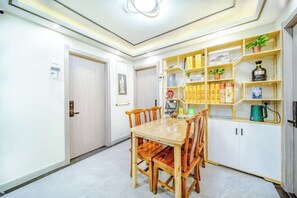 A dining area with a wooden table and chairs, a bookshelf with various items, and a door to another room.