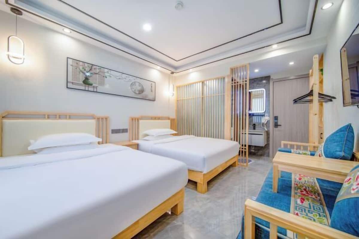 A hotel room with two beds, a sofa, a desk, and a bathroom visible through a partition.