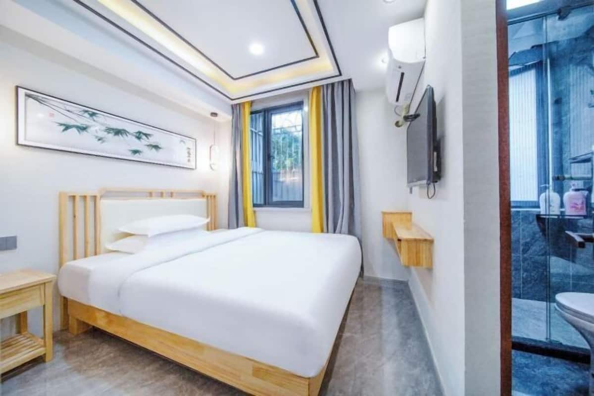 A modern hotel room with a bed, bedside table, artwork, window, and a view of the outside.