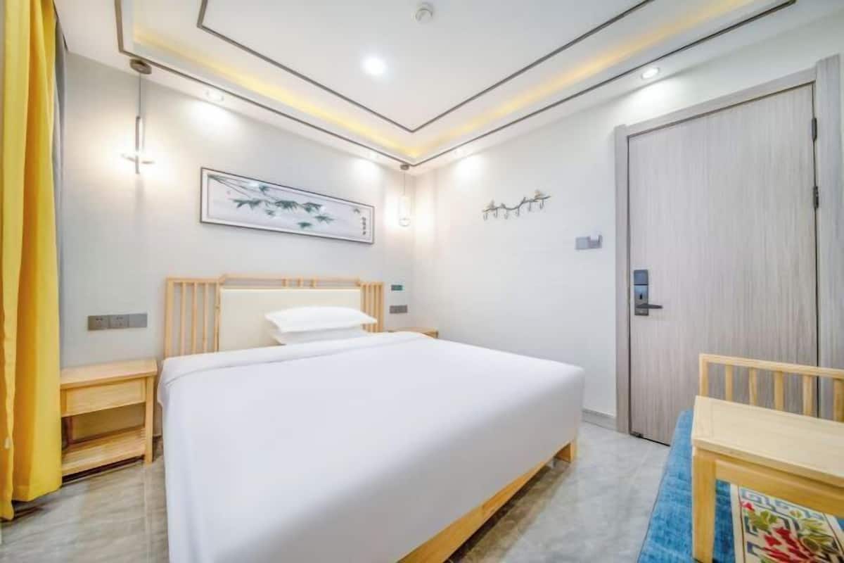 A modern hotel room with a large bed, bedside table, and a door.