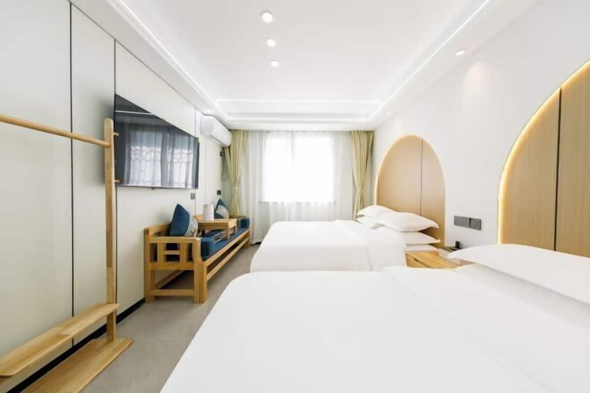 A hotel room with two beds, a seating area, a TV, and a window with curtains.