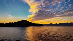 A sunset over a calm body of water with a silhouette of a mountain and a person standing on a hill.