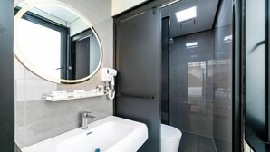 A modern bathroom with a white sink, a round mirror, a handheld showerhead, and a glass shower enclosure.