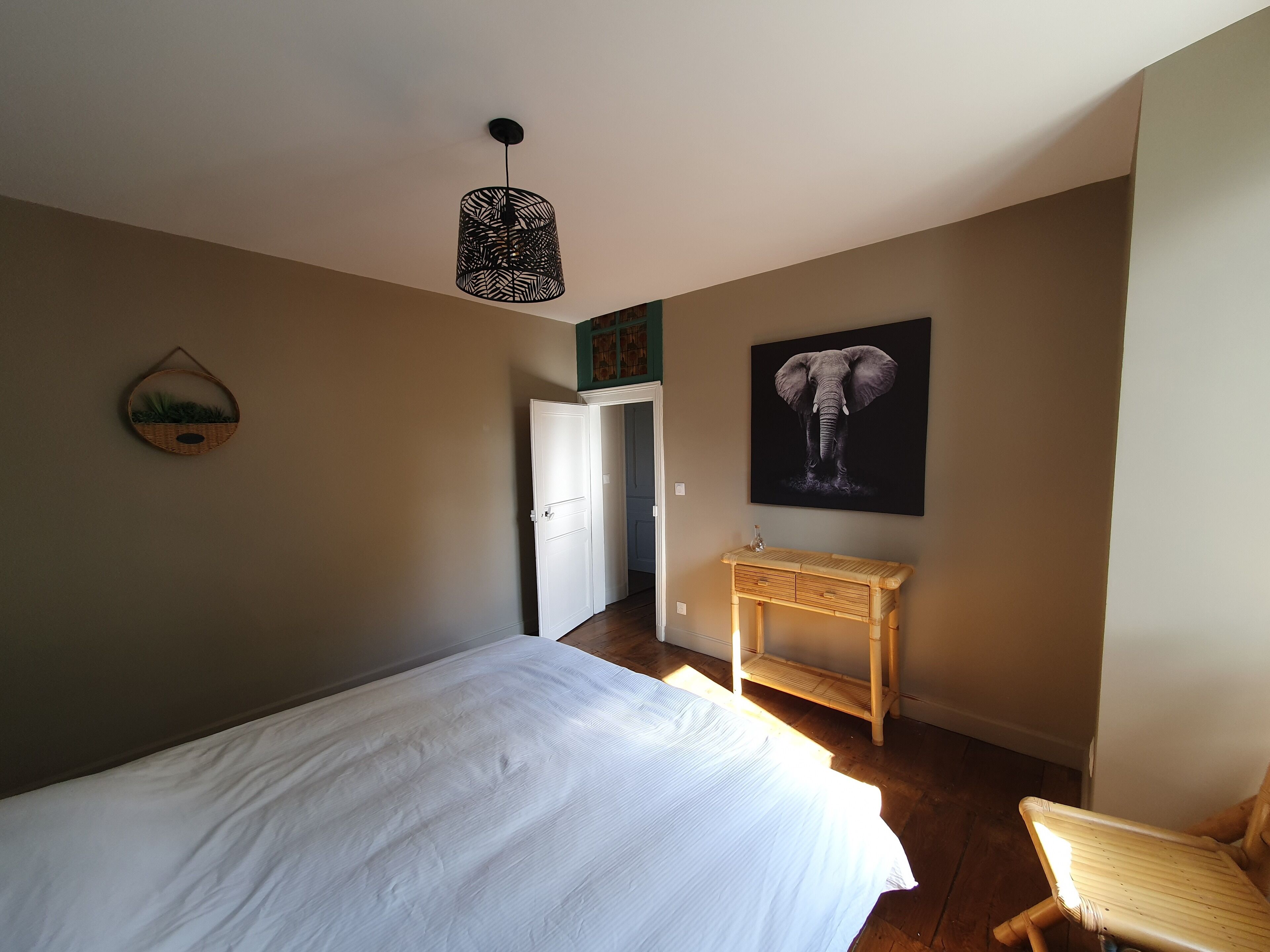 Een slaapkamer met een bed, nachtkastje, stoel, hanglamp en een aan de muur bevestigd schilderij.