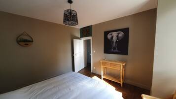 Een slaapkamer met een bed, nachtkastje, stoel, hanglamp en een aan de muur bevestigd schilderij.
