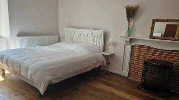 A bedroom with a white bed, a brick fireplace, and a white radiator.