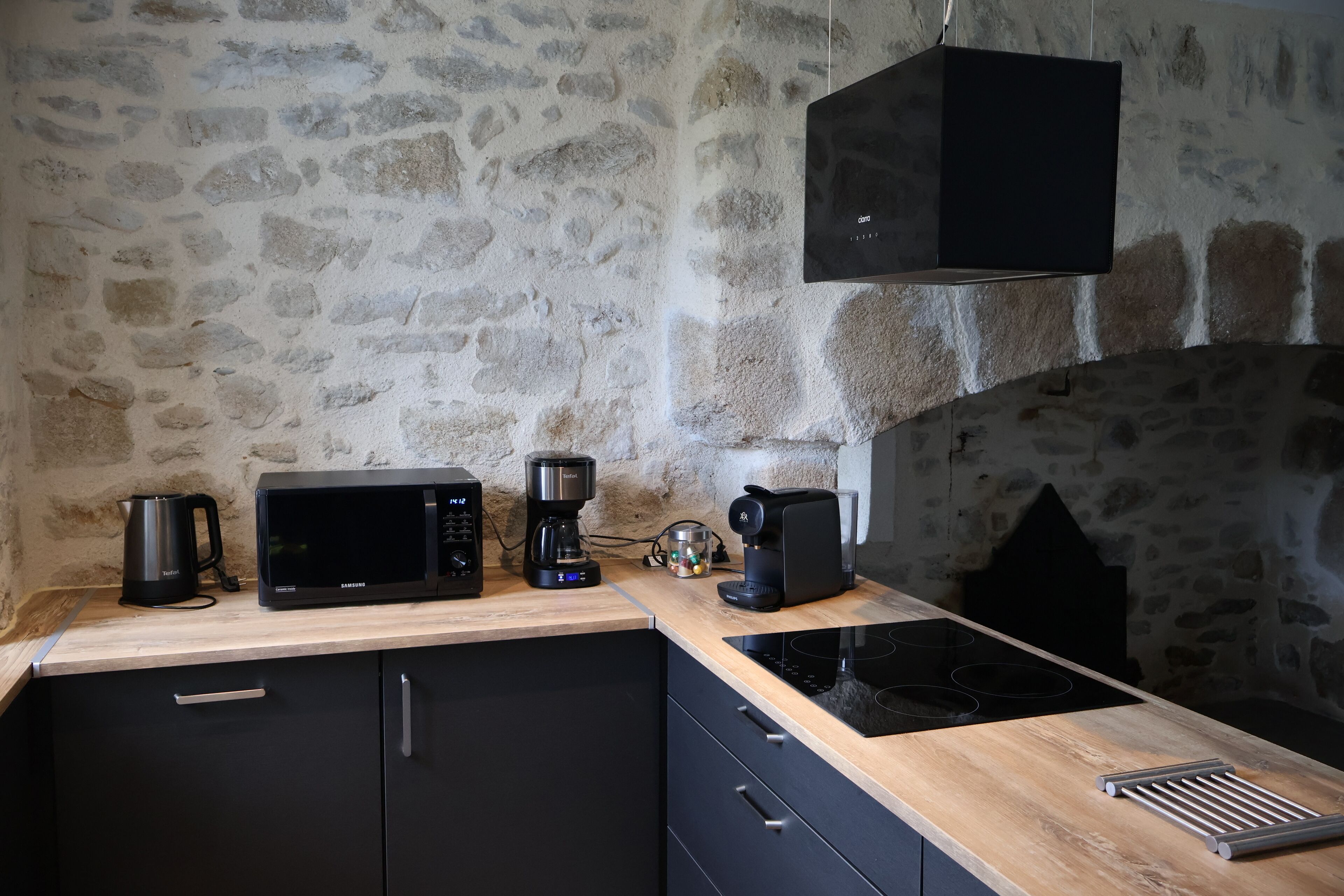 Una cocina con pared de piedra, microondas, cafetera y hervidor sobre una encimera de madera.