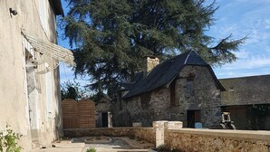 A courtyard with stone flooring, a large tree, and stone buildings. - Maison Rénovée Avec Terrasse + Parc Avec Piscine Chauffée et Terrasse Couverte (Estivaux)