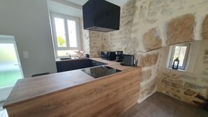 A modern kitchen with a wooden island, stone walls, and a built-in stove. - Maison Rénovée Avec Terrasse + Parc Avec Piscine Chauffée et Terrasse Couverte (Estivaux)