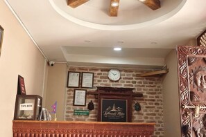 A reception area with a brick wall, a clock, framed certificates, and a wooden counter. - Hotel Vacation Home (Kathmandu)