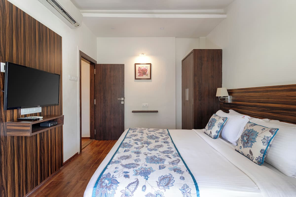 A bedroom with a large bed, wooden wardrobe, a flat-screen TV mounted on the wall, and a framed picture on the wall.