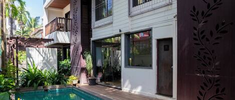 A swimming pool with a floating tray of food, surrounded by lush greenery and a multi-story building with balconies.
