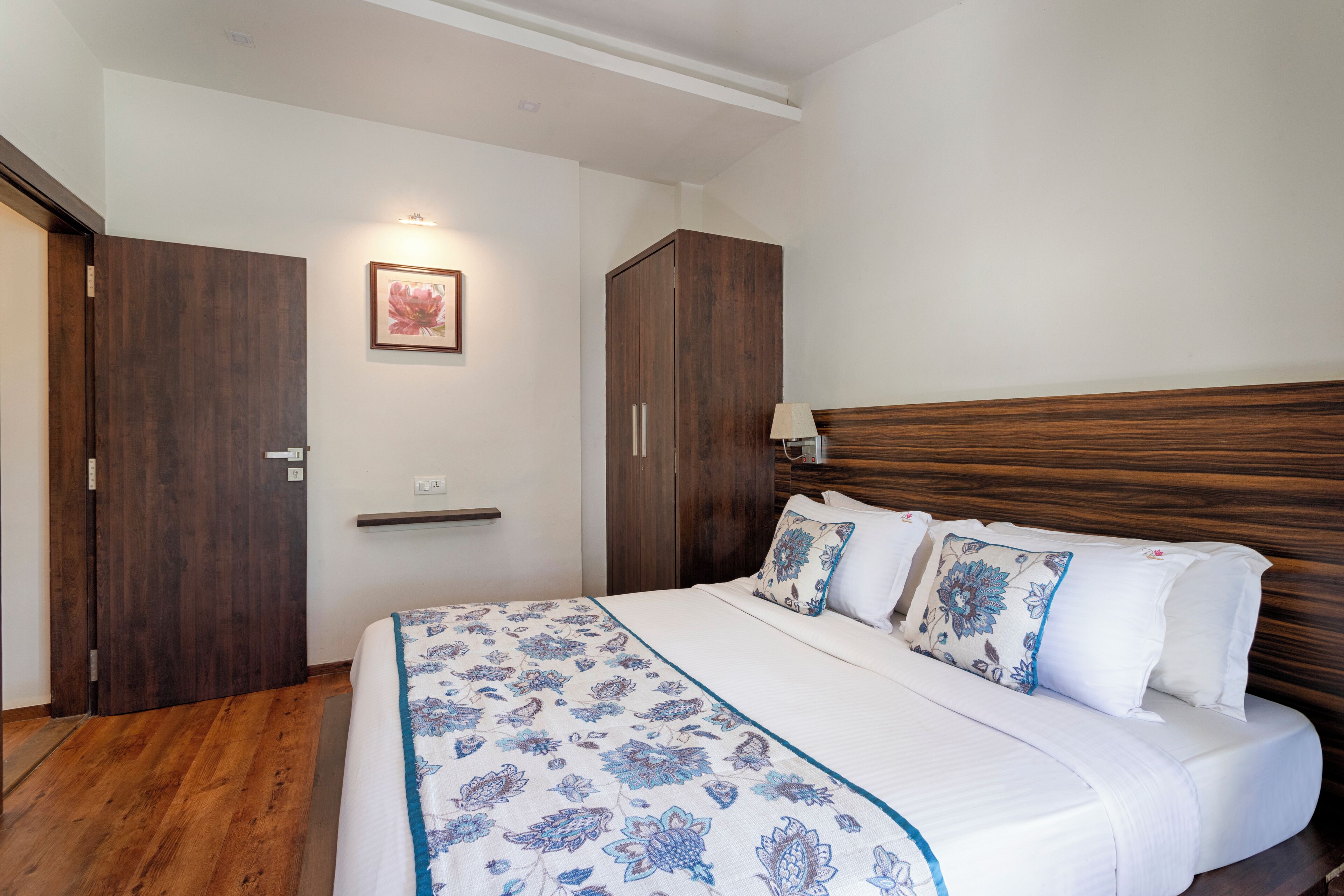 Une chambre à coucher avec une tête de lit en bois, un lit recouvert d’une literie à motifs floraux, une table de chevet avec une lampe et une armoire en bois.