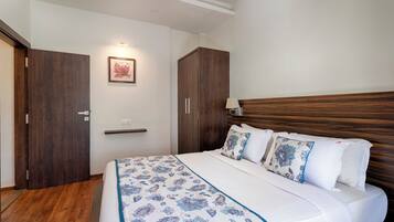 Une chambre à coucher avec une tête de lit en bois, un lit recouvert d’une literie à motifs floraux, une table de chevet avec une lampe et une armoire en bois.
