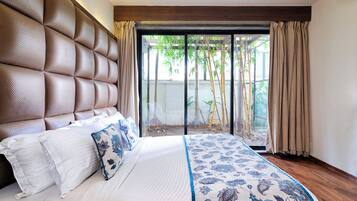 Un dormitorio con cabecera capitonada, una cama grande con ropa de cama blanca y azul estampada con motivos florales, y vista al bambú a través de una puerta corrediza de vidrio.
