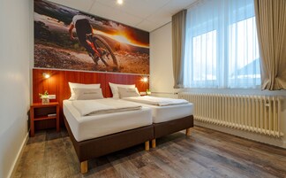 Camera d'albergo con un letto grande, un comodino, un termosifone e un'ampia finestra con tende.
