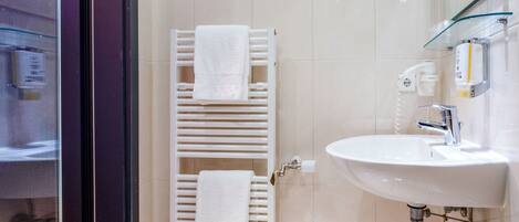 A bathroom with a white sink, a glass shower enclosure, and a towel rack with two white towels.