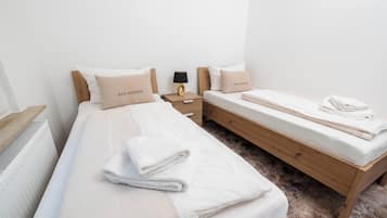 A hotel room with two beds, a wooden nightstand, a radiator, and a small table with a lamp.
