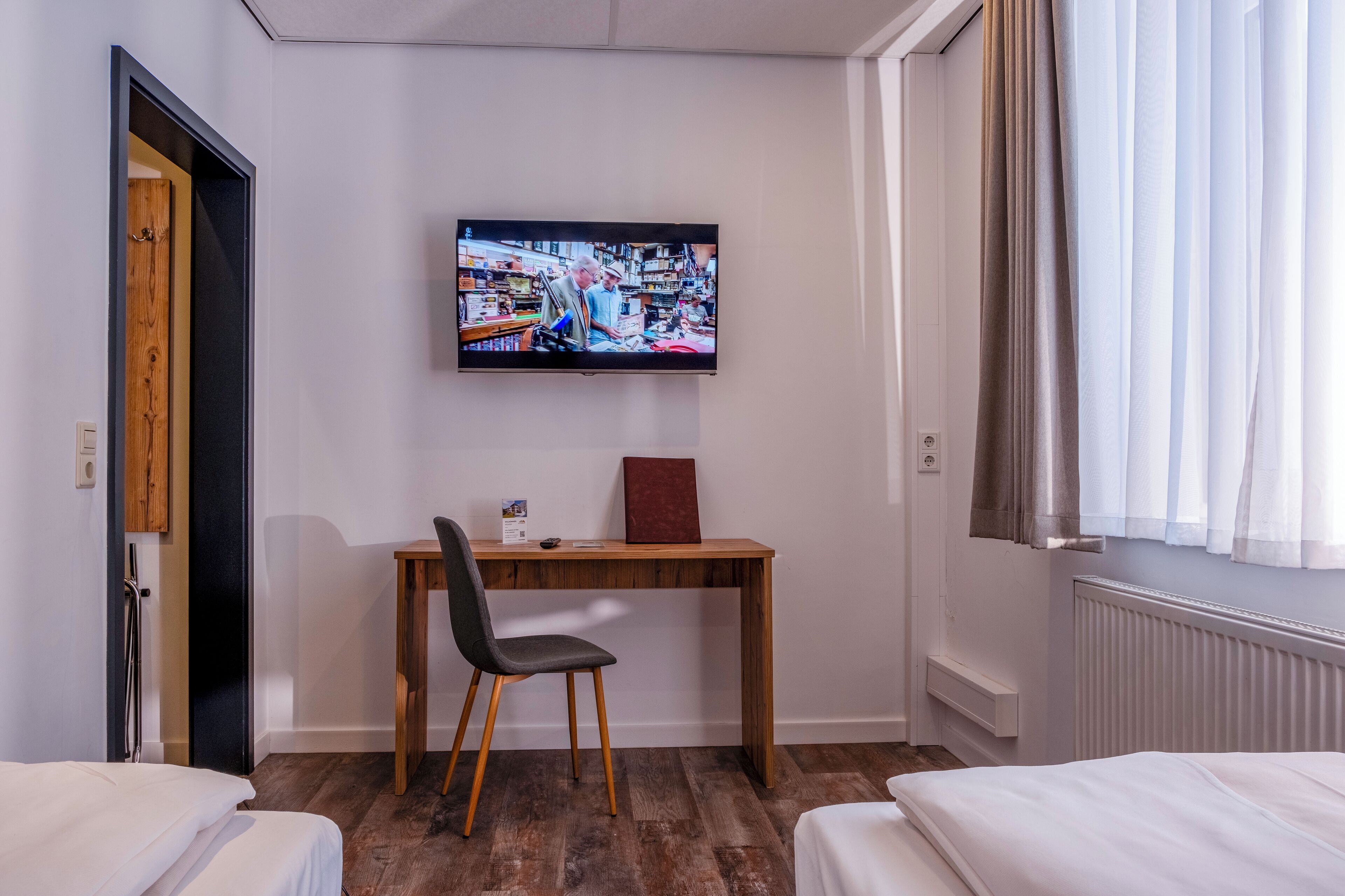 Una habitación de hotel con un escritorio de madera, una silla, una cama y un televisor instalado en la pared.