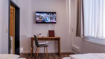 A hotel room with a wooden desk, a chair, a bed, and a TV mounted on the wall.