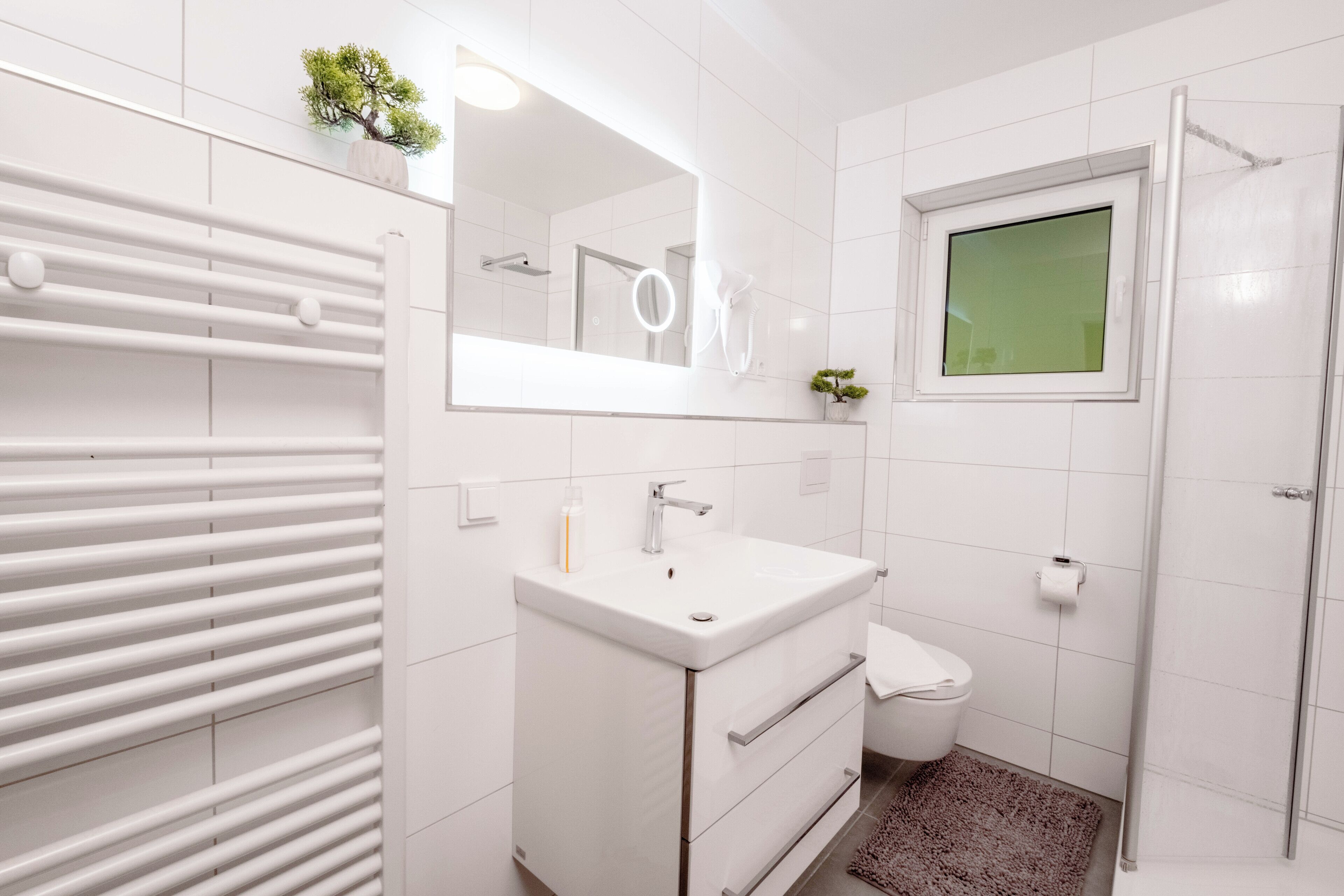 A modern bathroom with a white vanity, a mirror, a toilet, and a shower area.