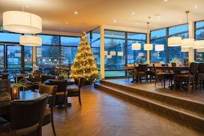 A modern dining area with a Christmas tree, wooden flooring, and large windows offering a view of the outdoors. - Hotel Winterberg Resort (Winterberg)