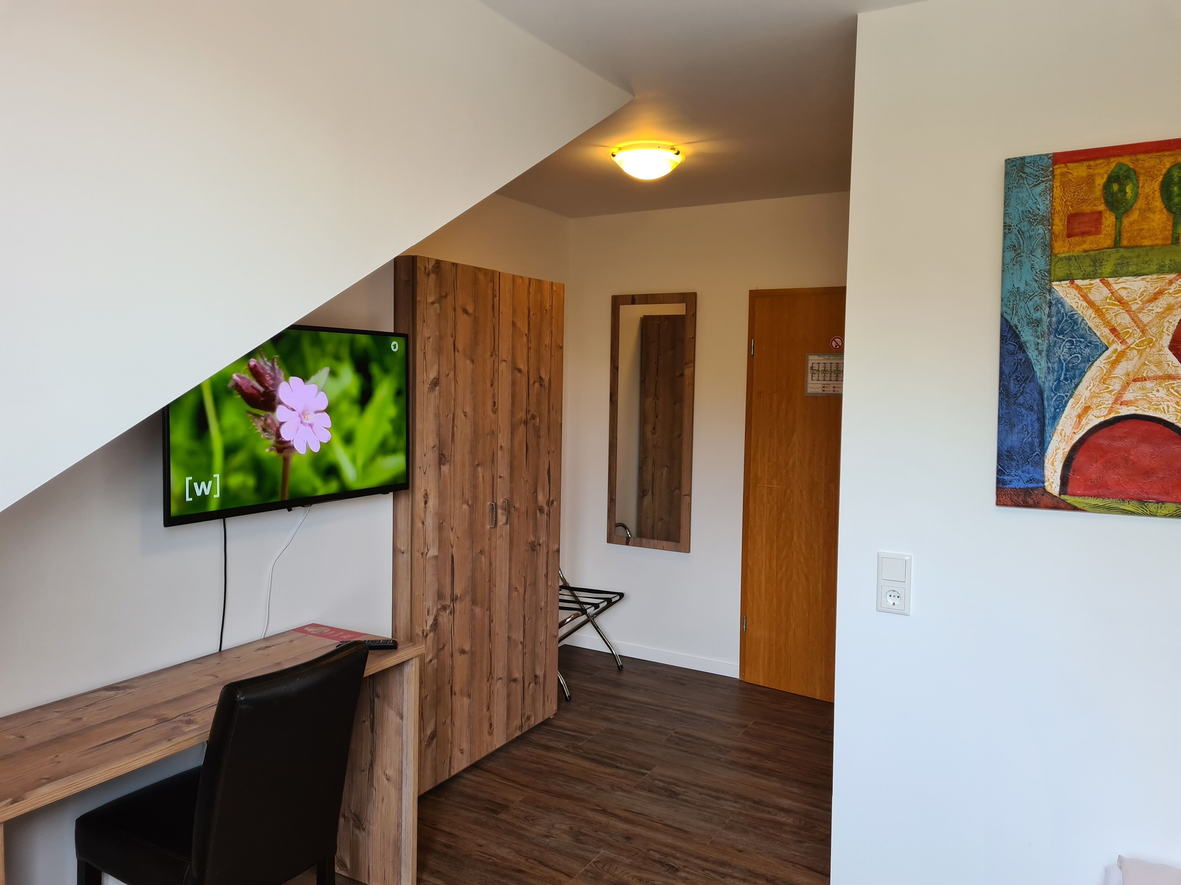 Ein modernes Wohnzimmer mit einem Holztisch, einem an der Wand montierten Fernseher und einem farbenfrohen abstrakten Gemälde.