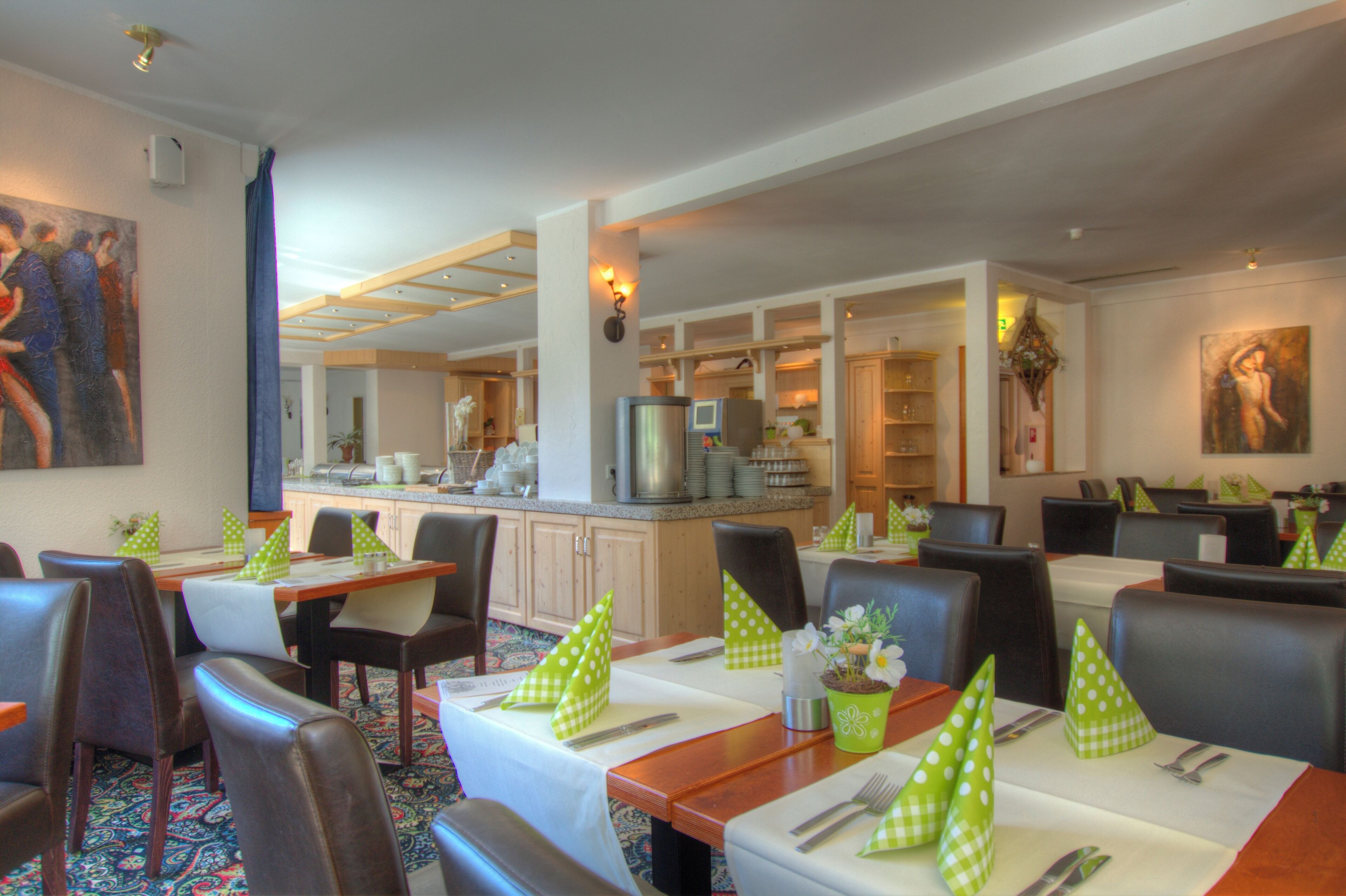 Un restaurante con mesas dispuestas para comer, sillas y una zona de cocina al fondo.