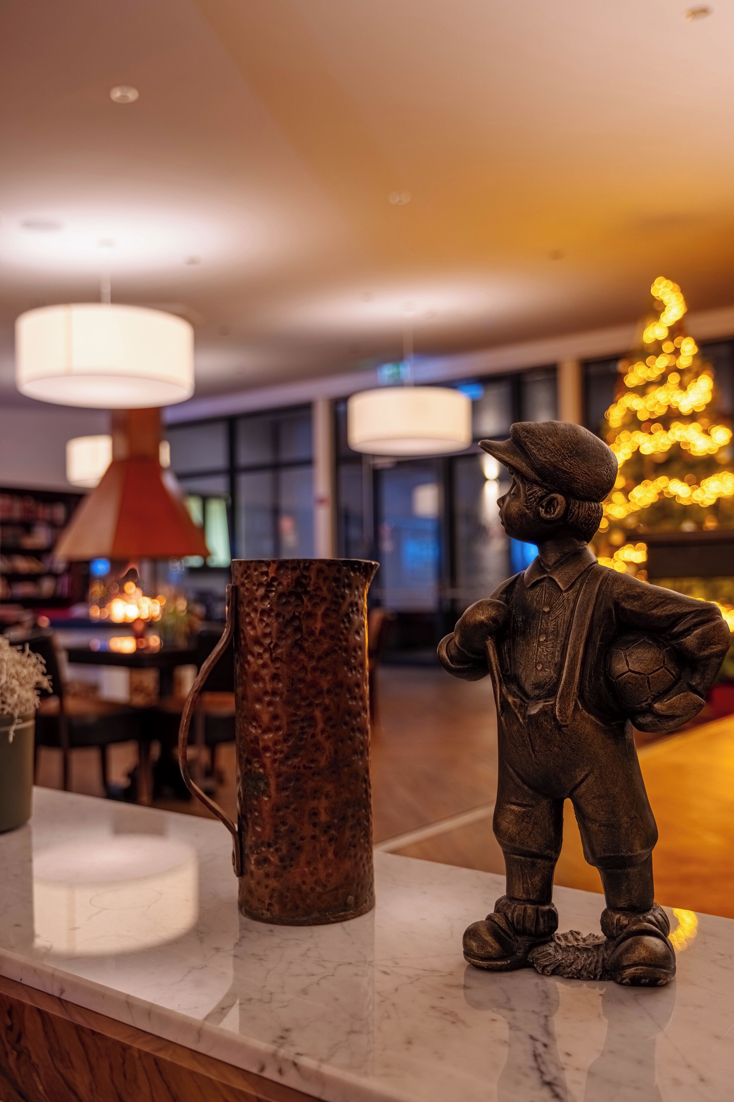Een beeld van een kind met een voetbal op een marmeren blad, een gegroefde metalen kan en een kerstboom met lichtjes op de achtergrond.