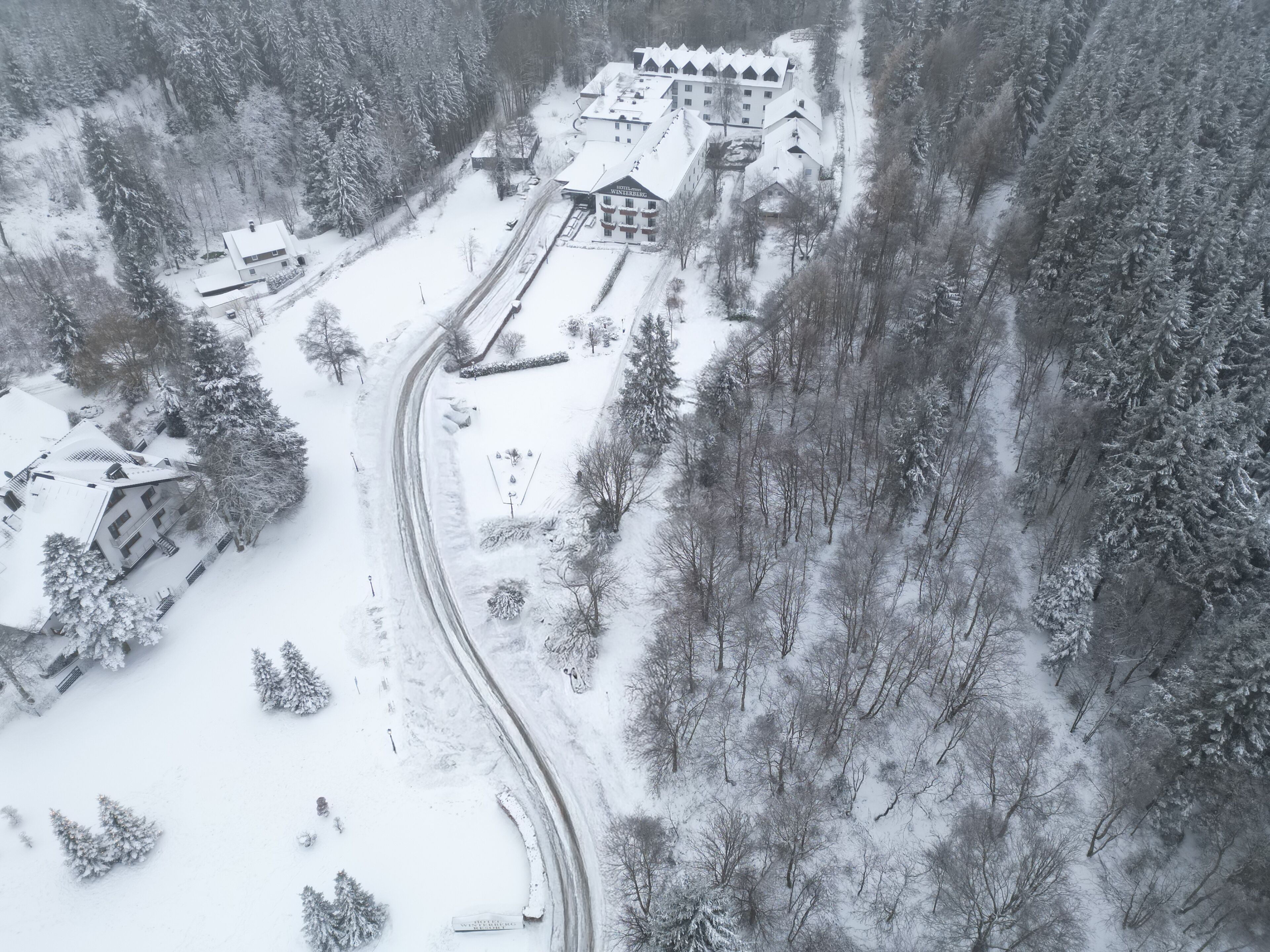 A snow-covered landscape with a hotel named "Hotel Winterberg" featuring a central building with multiple windows and a sloped roof.