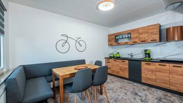 A modern kitchen with wooden cabinets, a dining table with chairs, and a wall-mounted bicycle art piece.