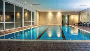 An indoor swimming pool with clear water, tiled walls, and a stone-textured wall in the background. - Hotel Winterberg Resort (Winterberg)