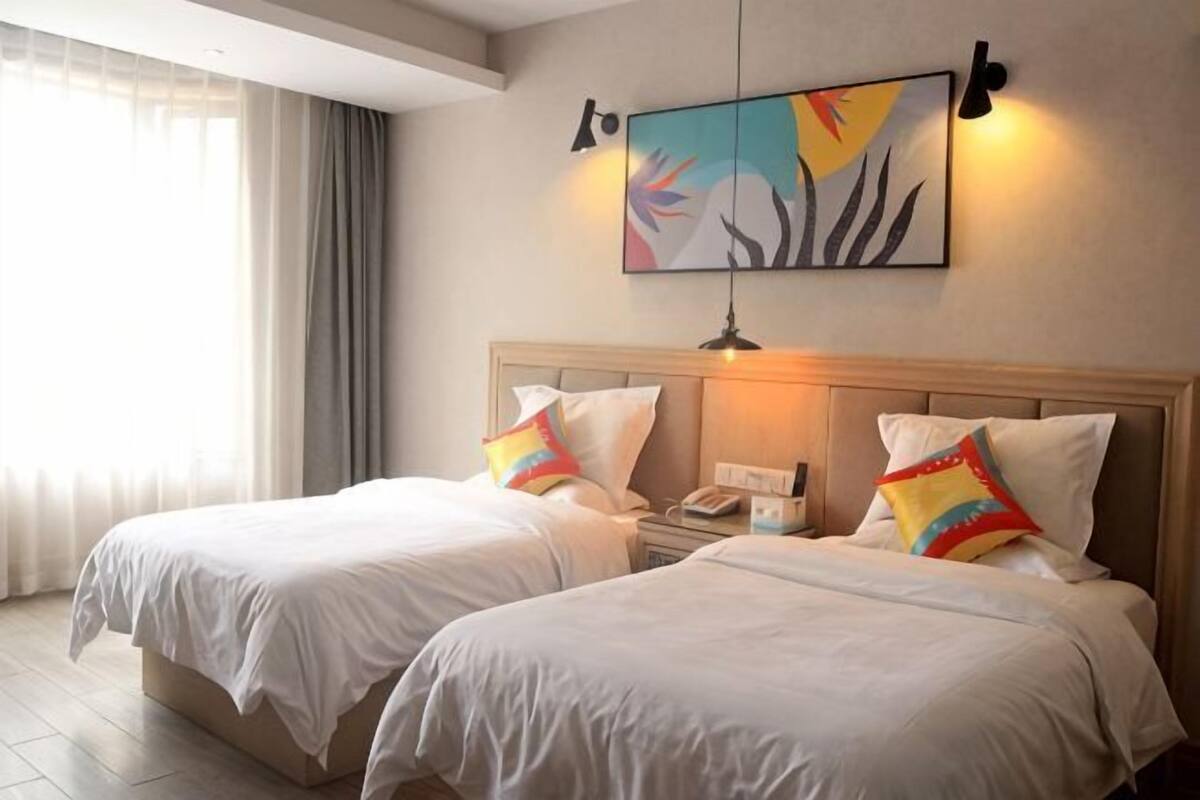 A hotel room with two beds, a nightstand, a lamp, and a painting on the wall.