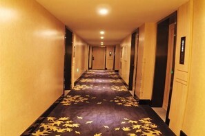 A hotel hallway with a carpet featuring a leaf pattern, doors on both sides, and a light-colored wall. - Pai Hotel (Xinchang Wanda Plaza store) (Xinchang)