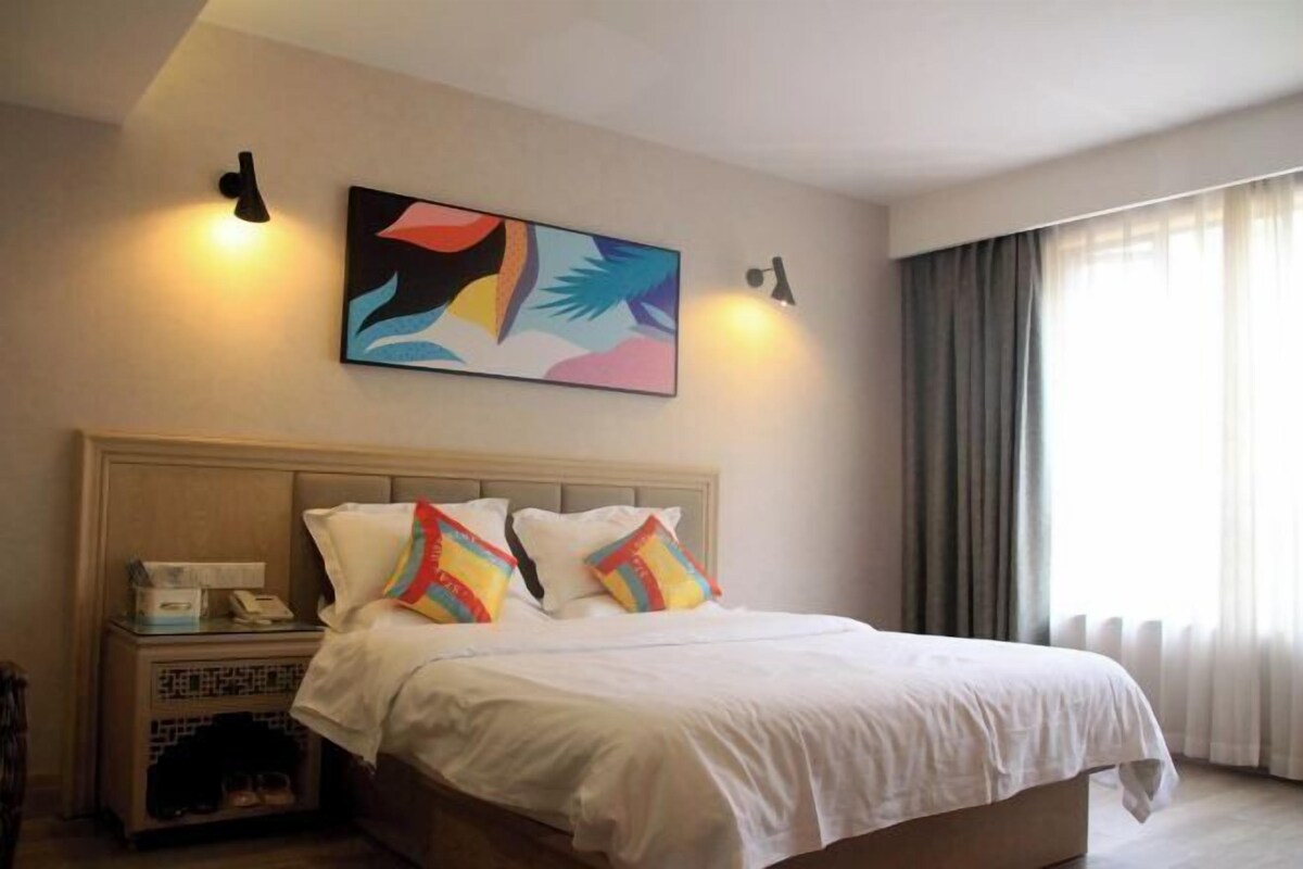 A hotel room with a bed, a nightstand, a telephone, a painting on the wall, and a window with curtains.