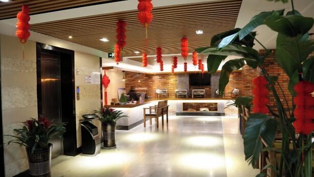 A hotel reception area with a modern design, featuring a reception desk, seating area, and a brick wall in the background. - Pai Hotel (Xinchang Wanda Plaza store) (Xinchang)