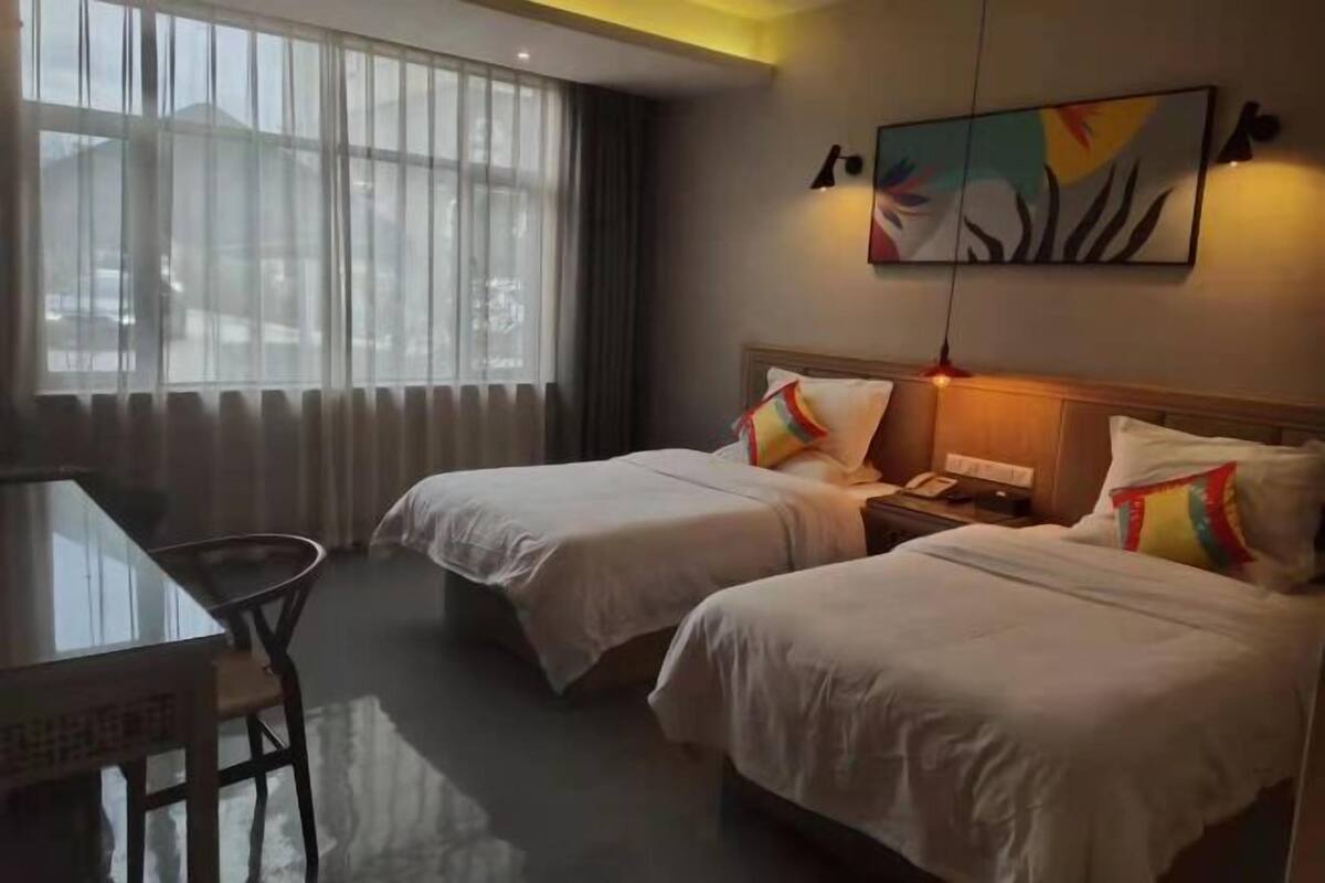 A hotel room with two beds, a desk, and a large window with curtains.