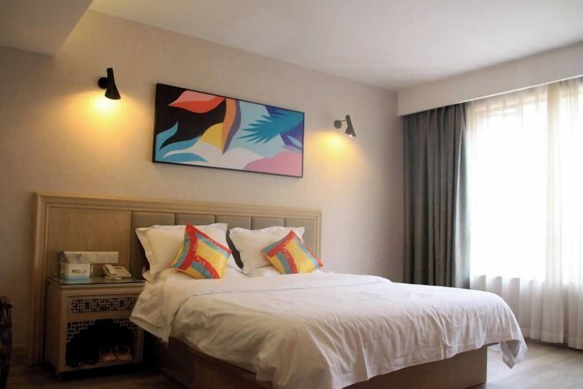 A hotel room with a bed, a nightstand with a phone, and a painting on the wall.