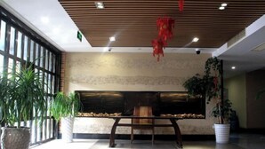 A lobby with a wooden ceiling, a fireplace, and potted plants. - Pai Hotel (Xinchang Wanda Plaza store) (Xinchang)