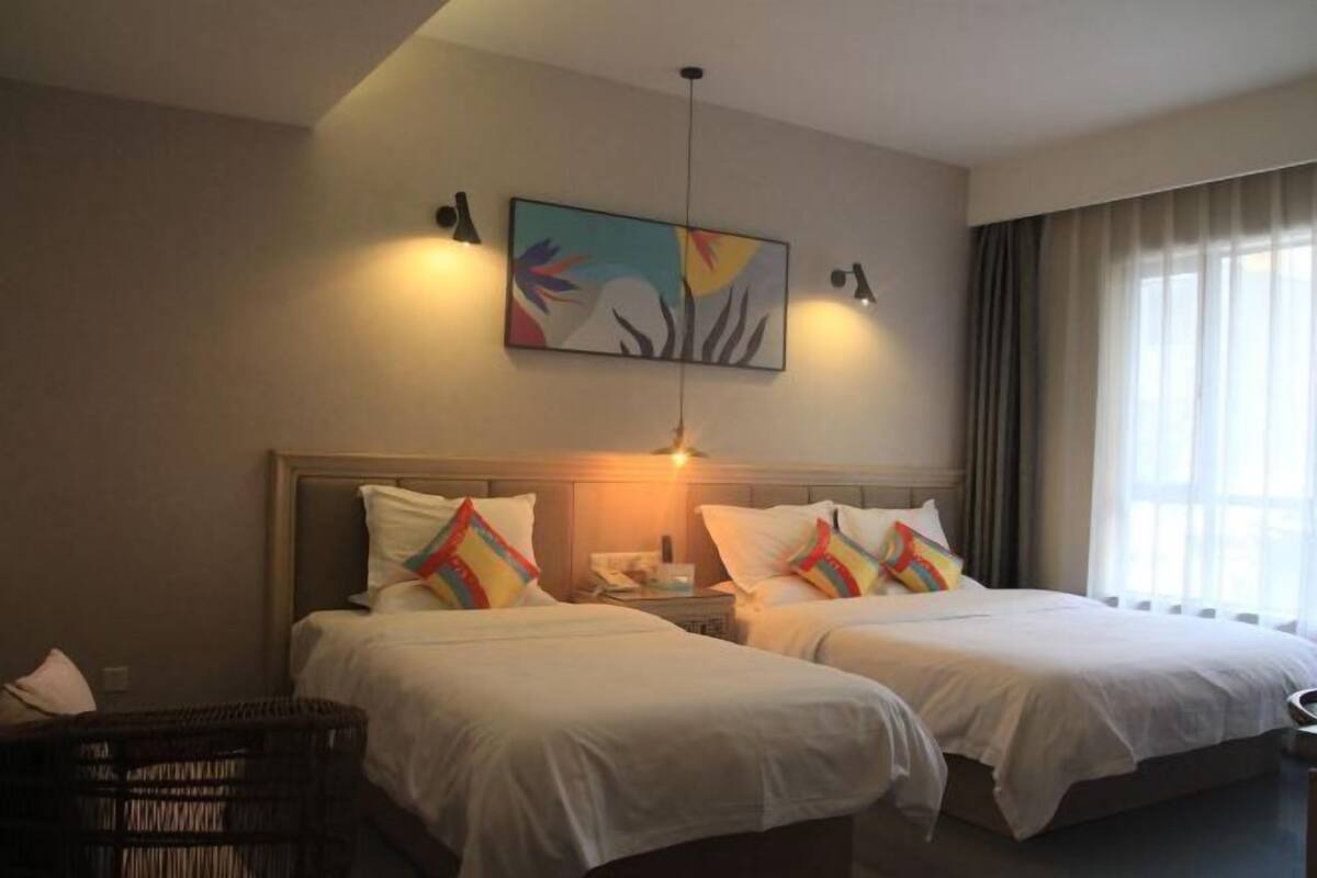 A hotel room with two beds, a painting on the wall, and a window with curtains.